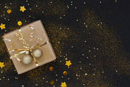 Christmas gift box or present decorated golden ribbon and two balls on black background with...