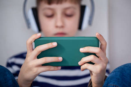 Child hands holding smartphone close-up for playing or learning. Kids hands looking at cellphone. Concept kids using technologyの写真素材