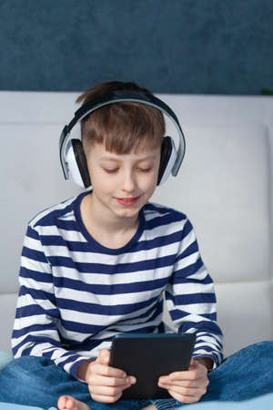 Cute child boy in headphone playing on a digital tablet on the bed in living room. Education, free...
