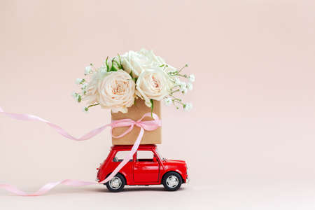Red car with a gift box of roses flowers on the roof on pink background. Happy Valentine's Day, Mother's Day, March 8, World Women's Day holiday card concept, flower delivery.の写真素材