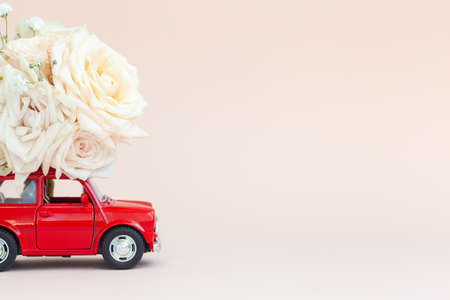 Red car with a roses flowers on the roof on pink background. Happy Valentine's Day, Mother's Day, March 8, World Women's Day holiday card concept, flower delivery.の写真素材