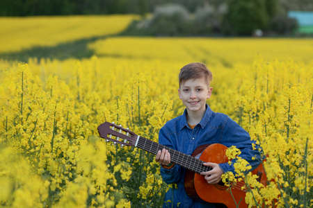 Portrait of cute boy playing a guitar in the summer yellow field. Portrait smiling childの写真素材