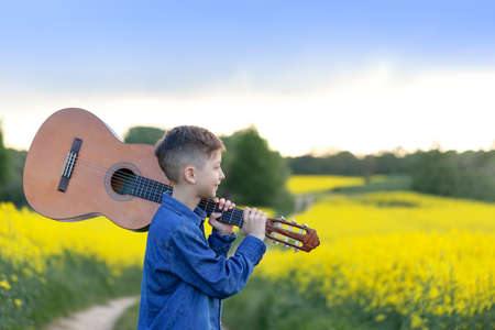 Portrait handsomeboy with guitar walking in the summer yellow field. Young musician on the road to...