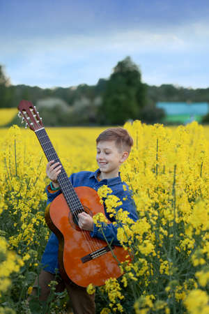 Portrait of cute boy playing a guitar in the summer yellow field. Child having fun imagining himself as a superstar.の写真素材