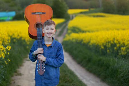 Portrait handsome boy with guitar walking on the summer road. Young musician on the road to success.の写真素材