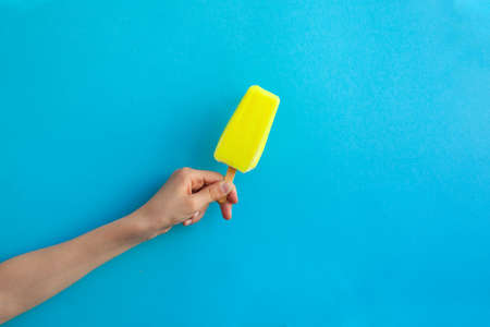 Child hand holding yellow lemon ice cream  on blue backgroundの写真素材