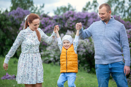 Happy family walking in the beautiful park. Parents holding the child's hands. Mom, dad and baby are happy to walk in summer day. Happy family concept.の写真素材