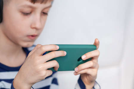 Smartphone in kid's hands. Boy play game on mobile phone. Kid holding Smartphone in hands closeup.の写真素材