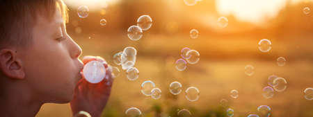 Child blowing soap bubbles on a summer day at sunset nature. Concept happy childhood. Banner.の写真素材
