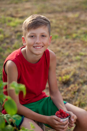 Smiling child holding full jar of fresh raspberries ready to eat on a summer day in the garden.の写真素材