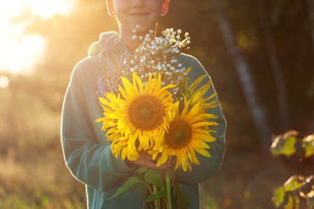 Cute kid boy holding bouquet of fields sunflowers in autumn sunset day. Child giving flowers. Autumn and thanksgiving concept.の写真素材