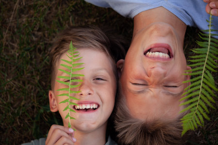 Close up portrait of two happy smiling brothers lying on green grass. Cheerful kids laughing together. Having fun.の写真素材