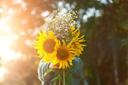 Cute kid boy holding bouquet of fields sunflowers in autumn sunset day. Child giving flowers. Autumn and thanksgiving concept.の写真素材