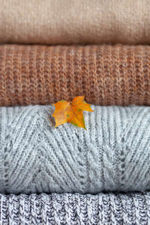 Closeup Stack of cozy knitted autumn and winter sweaters with yellow maple leaf on a neutral background. Concept of warmth and comfort clothes.の写真素材