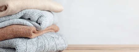 Stack of cozy knitted autumn and winter sweaters on a neutral background. Concept of warmth and comfort clothes. Bannerの写真素材