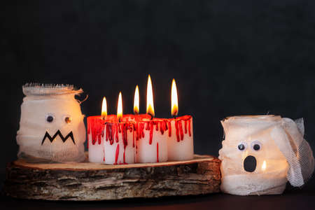 Burning bloody candles and mummy from a jar on darkness background. White candles covered in red wax like blood drops. Halloween holiday concept.の写真素材
