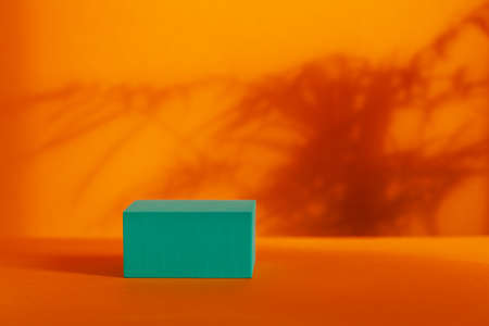 Turquoise podium with shadows leaves on orange background. Concept scene stage showcase for product, promotion, sale, banner.の写真素材