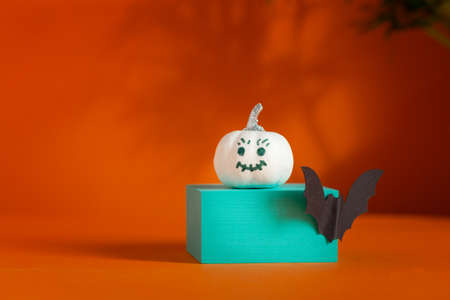 White pumpkin with face on podium over orange background with shadows and copy space. Holiday Halloween party concept.の写真素材