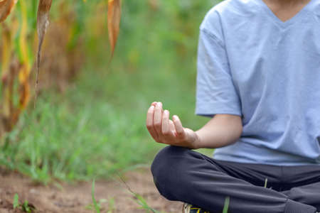 Closeup of kid hand meditating on nature. Kid boy Half Lotus pose yoga meditating on grass in summer day. Health, meditation and relaxation concept.の写真素材