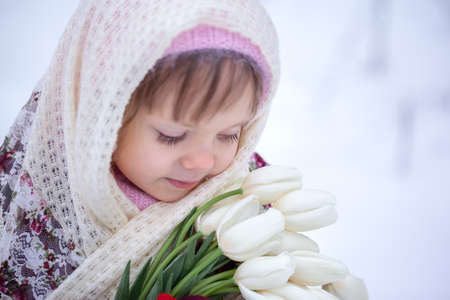 Close up winter portrait of adorable little caucasian girl with white tulips in winter park.の写真素材