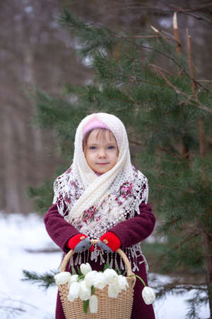 Cute little girl holding a basket full of white tulips in the winter forest.の写真素材