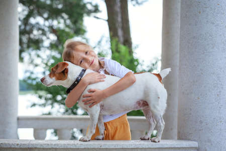 Little girl hugging Jack Russell Terrier dog in nature. Beautiful dog. Kid and dog friendship. A special bond between the kid and its dog. Love and affection.の写真素材