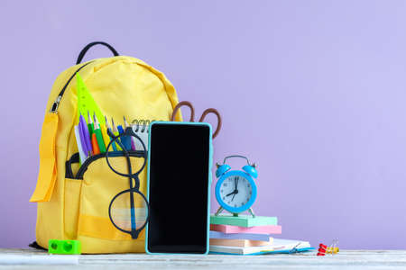 concept back to school. Full yellow school backpack and smartphone, eyeglasses, alarm clock with...