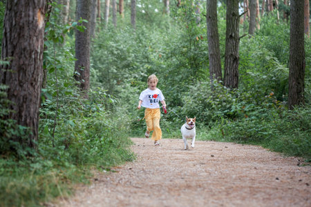 Carefree child with dog running on walkway in forest summer day. Happy girl running with pet Jack Russel.の写真素材