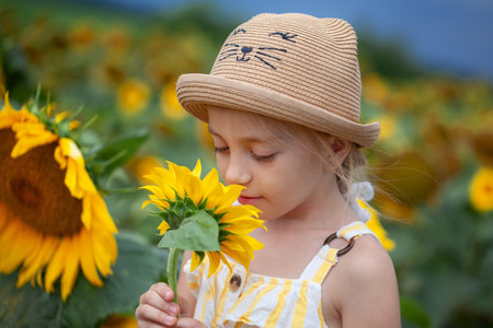 Adorable little girl in a straw hat smelling a sunflower on the field. Summer cozy mood.の写真素材
