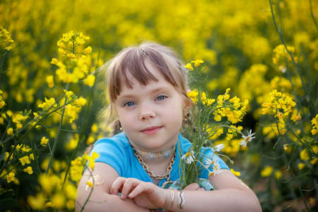 Portrait of a cute girl kid in a yellow rape flower field in summer day. A child in a blooming meadow. Authenticity, rural life, eco-friendlyの写真素材