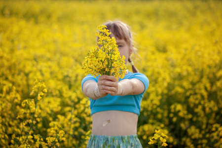 Happy child girl with bouquet of wild yellow flowers in his hands enjoying summer day. Concept child...
