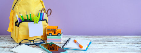 Banner. concept back to school. Full yellow School Backpack with stationery on table on purple...