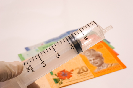 hand holding disposable medical syringe with bank notes as blurry background