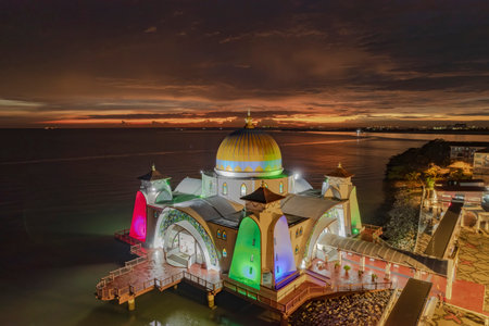 A stunning aerial view of the Strait Mosque at twilight, showcasing its intricate architecture and vibrant lighting against the backdrop of the tranquil sea.の写真素材