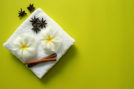 White towel with flowers of plumeria with stars of anise and cinnamon sticks on the yellow background for spa theme.の写真素材