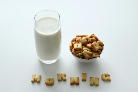 A glass of milk, a bowl of cookies with inscription from the cookies on the white background.の写真素材