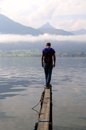 Travel to Sankt-Wolfgang, Austria. The young man are walking on a bridge with the view on the lake near to mountains in the cloudy weather.の写真素材