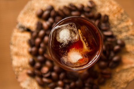 A glass of ice coffee on the wooden background with coffee beans.