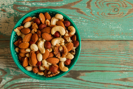 Mixed nuts in a turquoise bowl on a turquoise wooden background.