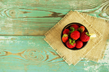 A metal cup with strawberries on the napkins from sackcloth on the blue-white wooden background.の写真素材