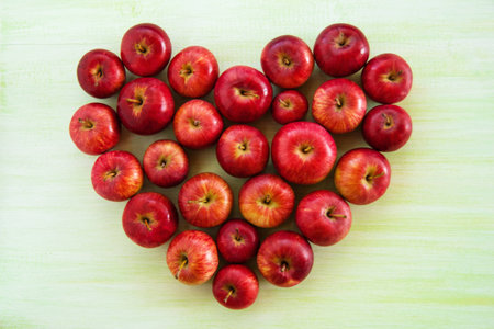 A heart from ripe red apples on the green wooden background, top view.の写真素材
