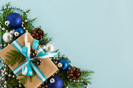 Christmas flat lay composition of fir branches with gift box and decorations at the left bottom corner with copy space on the blue background.の写真素材