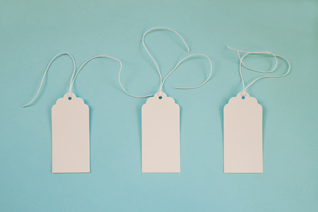 Three white blank paper price tags or labels set on the blue background, top view.の写真素材