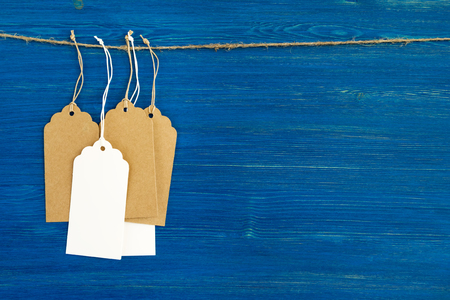 Brown and white blank paper price tags or labels set hanging on a rope on the blue wooden background.の写真素材