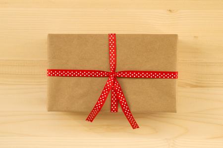 Gift box wrapped of craft paper and red ribbon on the wooden background, top view.