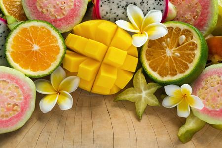 Bright colorful tropical fruits (mango, tangerine, guava, dragon fruit, star fruit, sapodilla) with flowers of plumeria on the wooden background.の写真素材