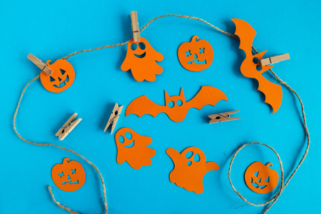 Preparation for Halloween. Orange paper decorations - ghosts, pumpkins and bats on a rope with pins on a blue background, top view.の写真素材
