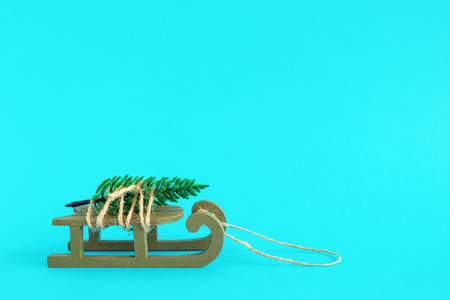 Green wooden sleigh with tied artificial fir tree on a bright blue background. Christmas and New...
