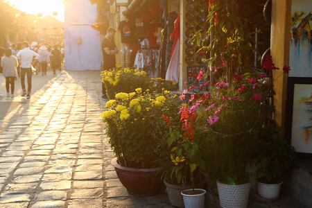Hoi An, Vietnam - February 17, 2018: Touristic street in old historical town with shops, colorful flowers and walking tourists at the sunset.のeditorial素材
