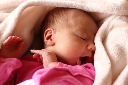 Cute newborn baby in pink baud with an open mouth on her bed under beige blanket.の写真素材